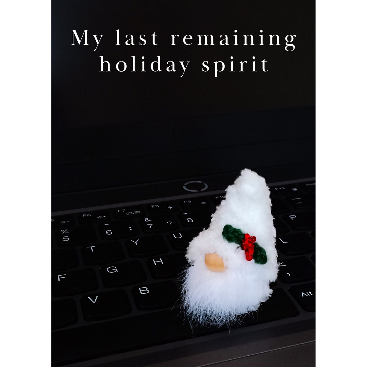 A humorous office Secret Santa digital card. A tiny pocket-sized white holiday amigurumi gnome with a small green holly leaf sits on a black computer keyboard. The minimalist white text reads: 'My last remaining holiday spirit'.