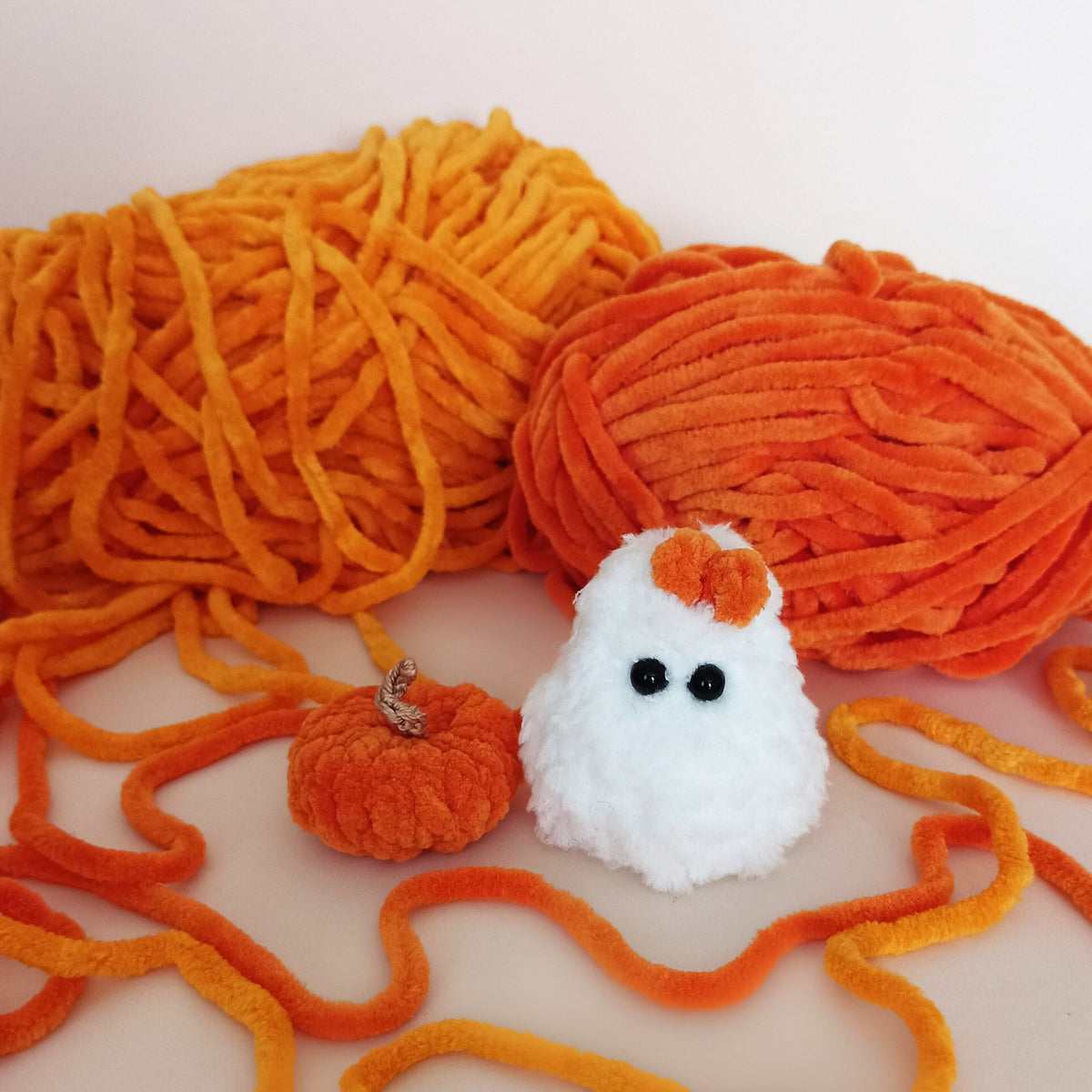 Handmade white crochet ghost with orange bow and tiny pumpkin surrounded by soft orange yarn, cozy Halloween decor