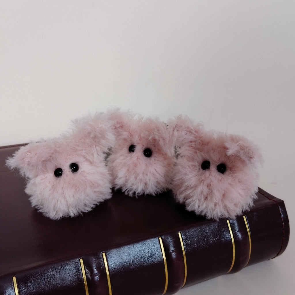 Three tiny fluffy pink handmade bunny desk friends sitting together on a dark brown book