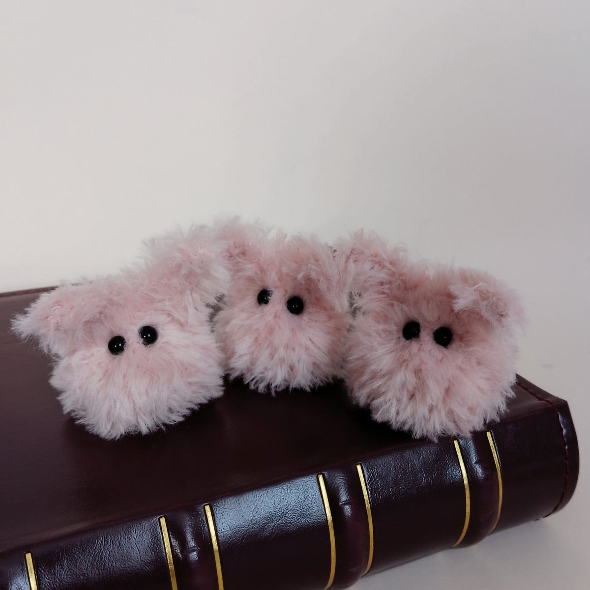 Three tiny fluffy pink handmade bunny desk friends sitting together on a dark brown book