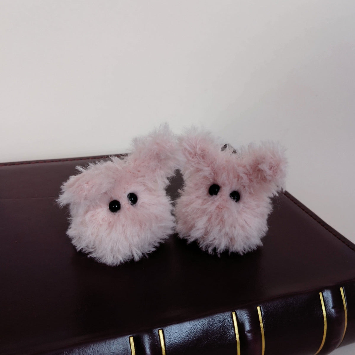 Two tiny pink fluffy handmade bunny desk friends sitting on a dark brown book