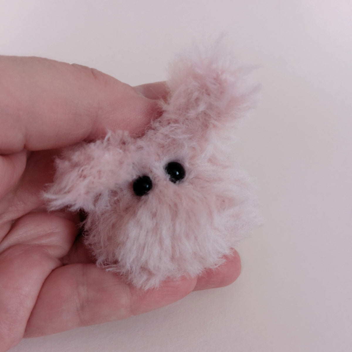 Tiny pink fluffy handmade bunny desk friend held in a hand to show its small size