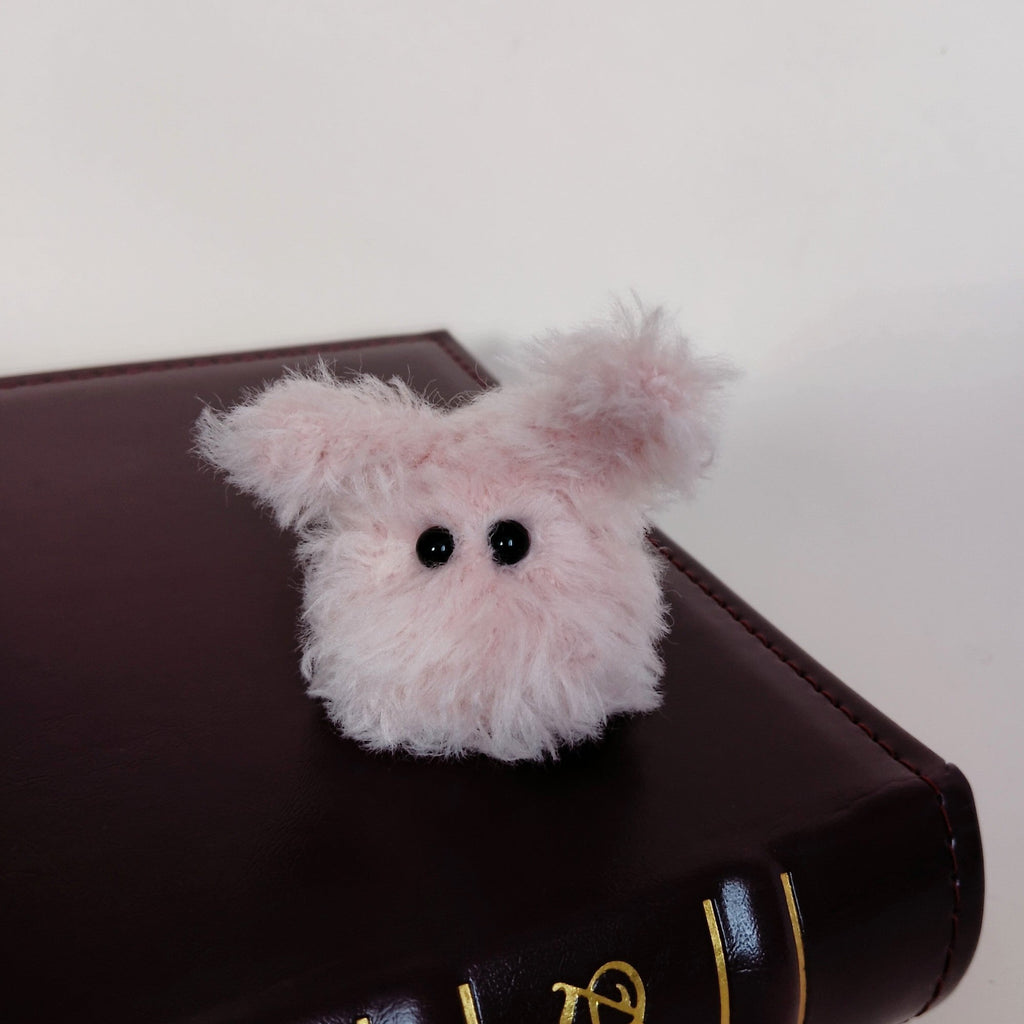 Tiny pink fluffy handmade bunny desk friend sitting on a dark brown book