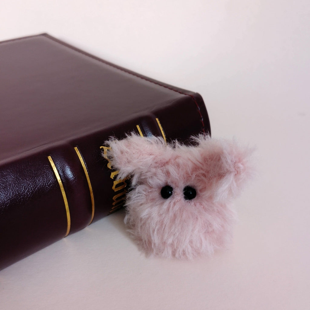 Tiny pink fluffy handmade bunny desk friend sitting beside a dark brown book