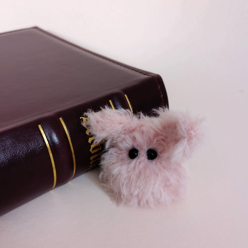 Tiny pink fluffy handmade bunny desk friend sitting beside a dark brown book