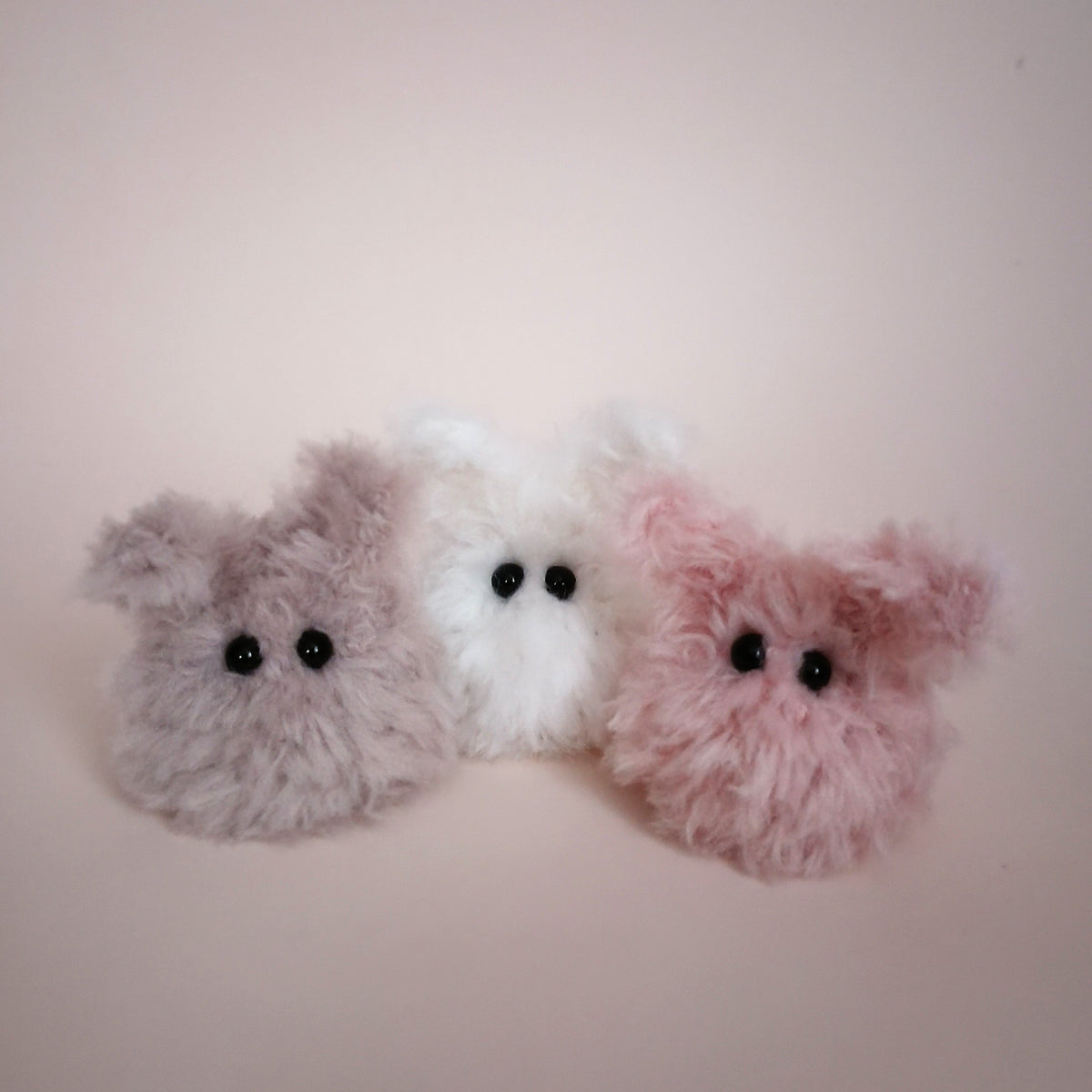 Three handmade Worry Bunnies in gray, white, and pink made from soft fluffy yarn sitting together