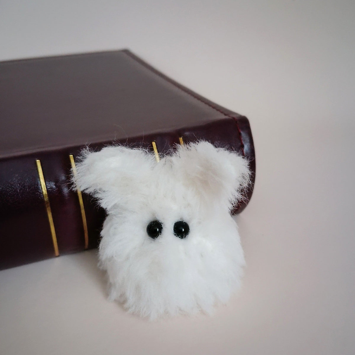 White Worry Bunny handmade from soft fluffy yarn sitting beside a dark brown book