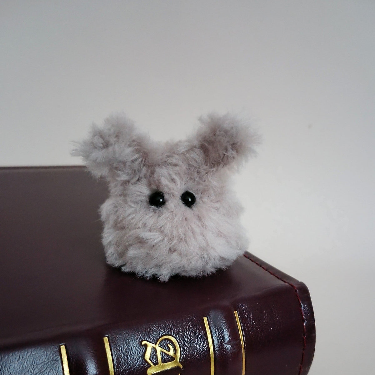 Tiny gray fluffy handmade bunny desk friend sitting on a dark brown book