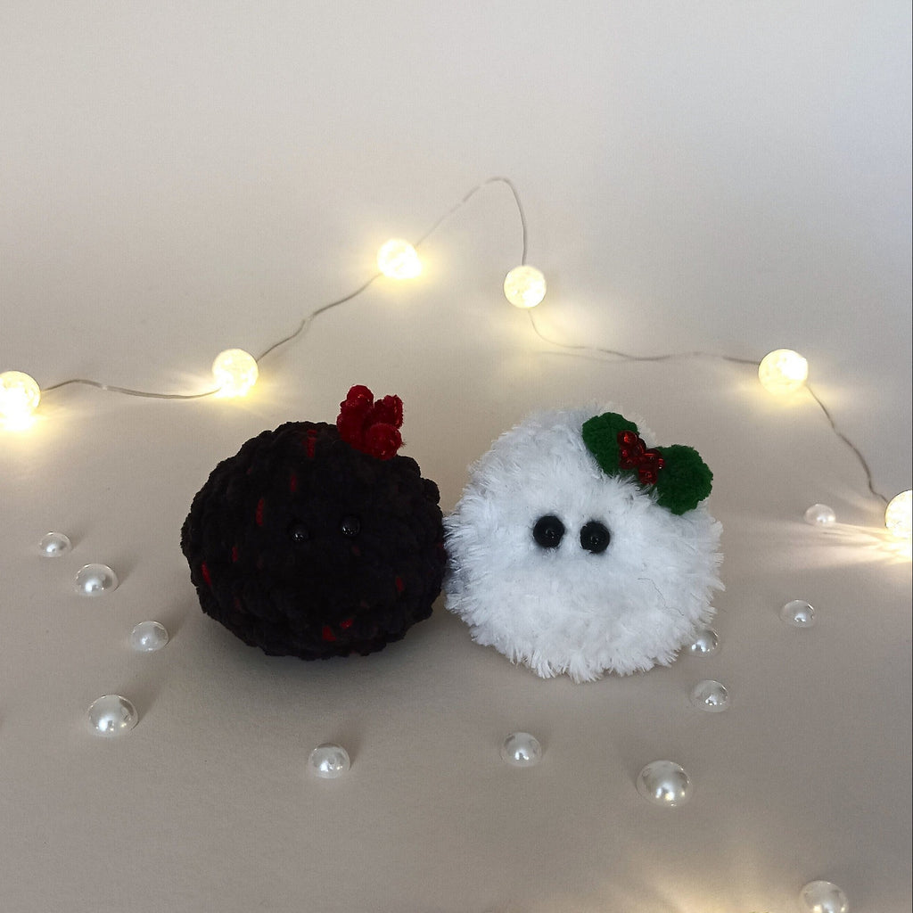 Tiny white crochet Christmas snowball and little black coal friend sitting together among warm fairy lights and pearl decorations.