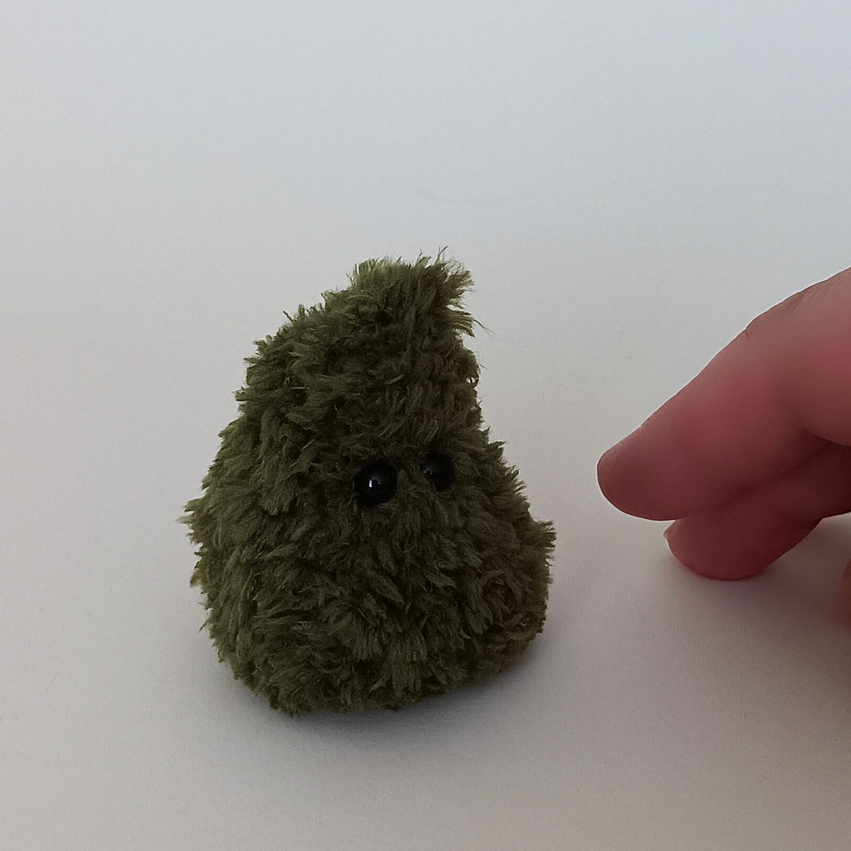 Tiny handmade green crochet Christmas tree shown beside a hand for scale, fluffy miniature desk and shelf companion