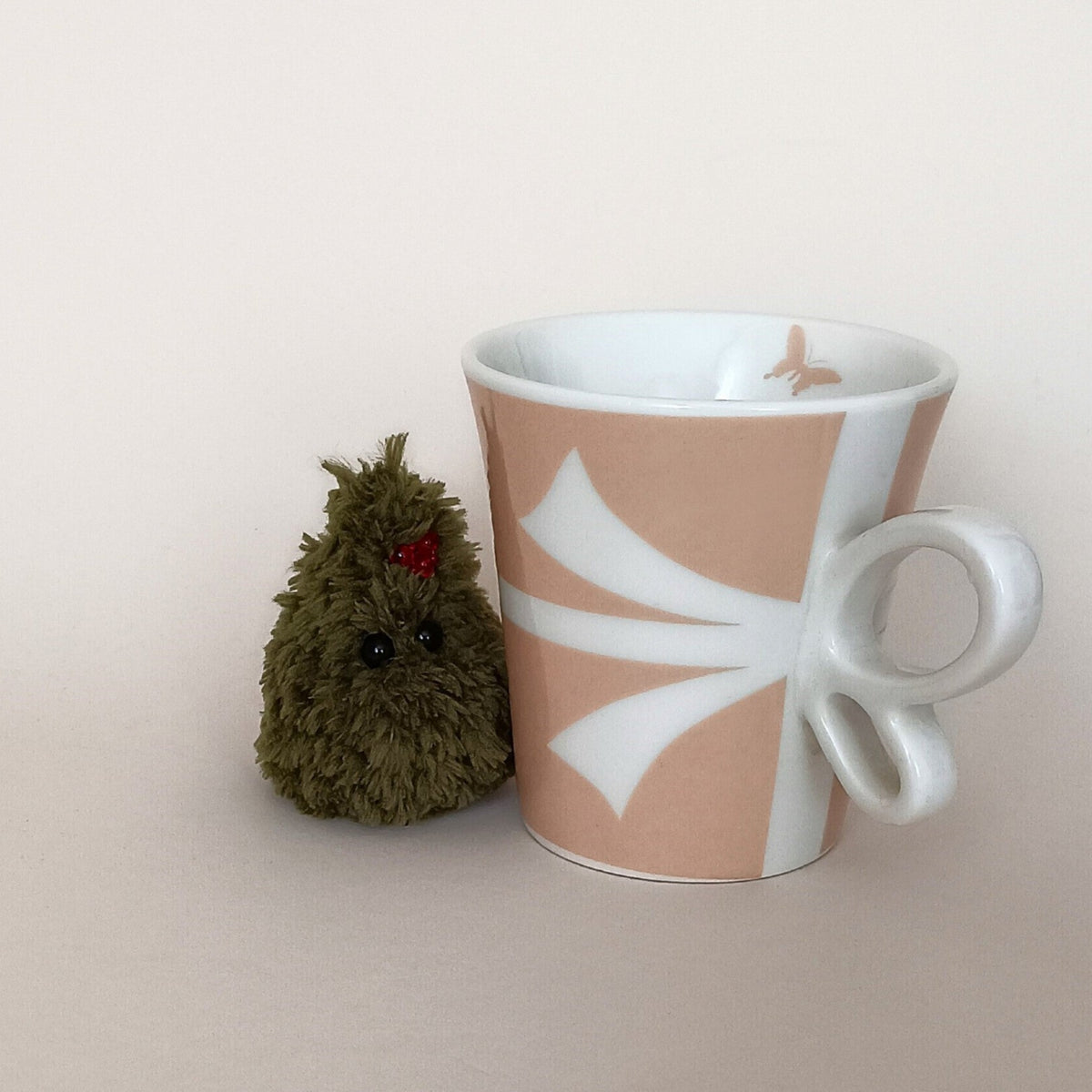 Tiny green crochet Christmas tree with red berry decoration beside a coffee cup, miniature holiday desk companion
