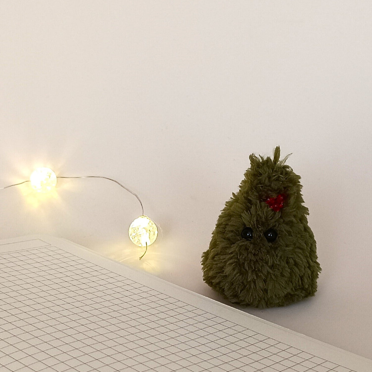 Tiny green crochet Christmas tree with red berry decoration beside a notebook and warm fairy lights, cozy holiday desk decor