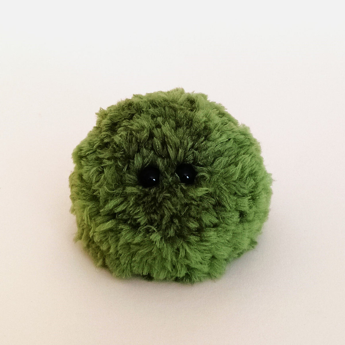 A single muted olive green fuzzy moss ball plush desk decor friend. Unique handmade micro crochet element for dark academia and nature inspired spaces.