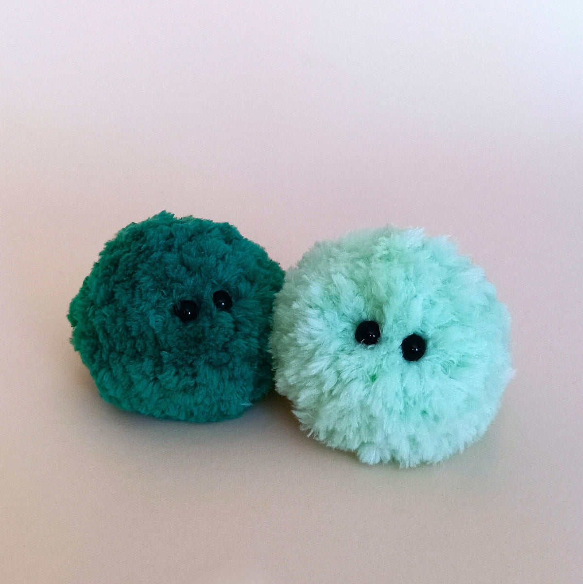 A dark forest green and a light teal fluffy moss plush buddy sitting together on a white background. Unique handmade gifts for stationery and cozy style lovers.