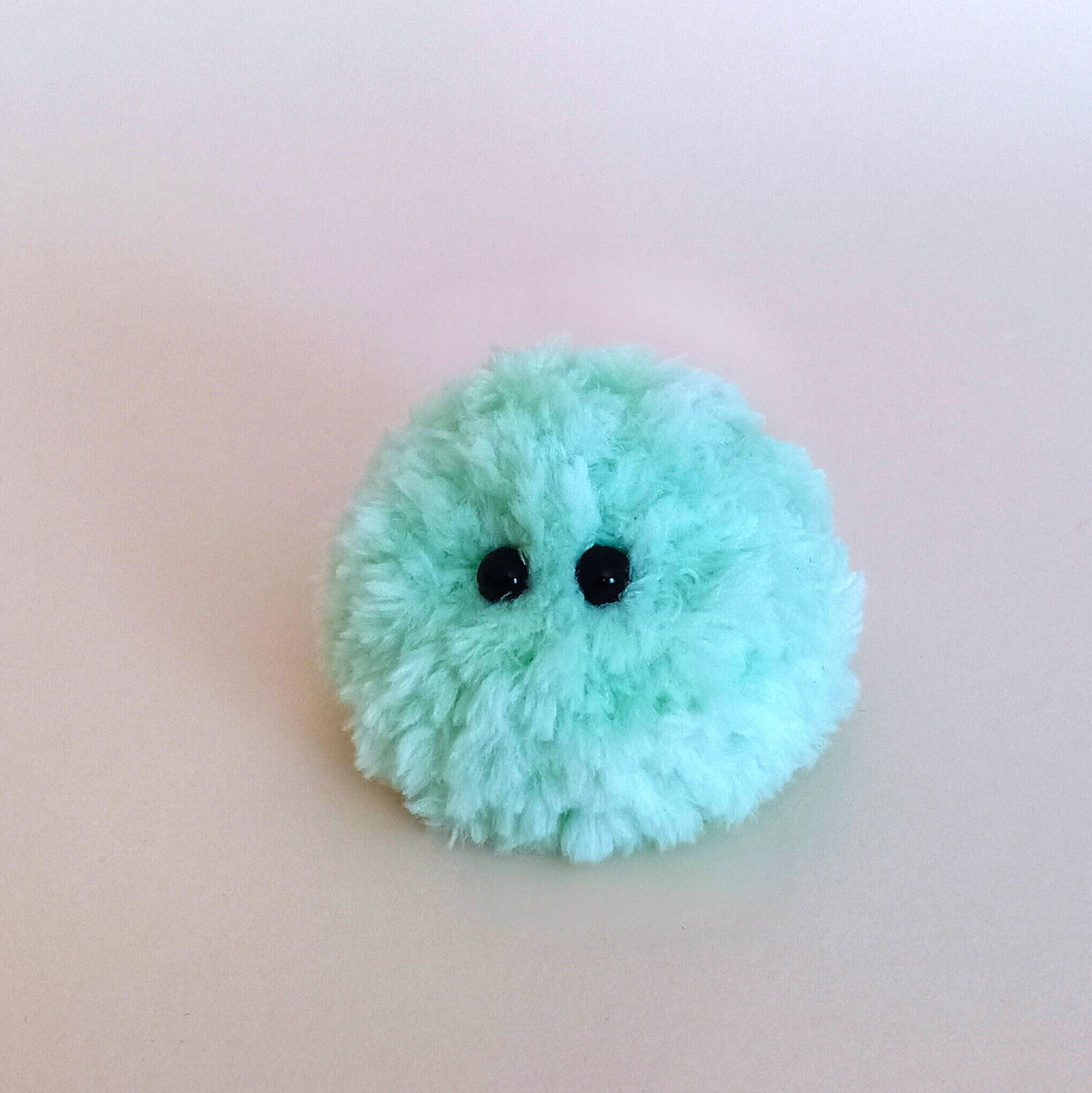 One tiny light mint green fuzzy moss ball desk pet with a cute face. Pocket-sized anxiety relief worry stone alternative and small gift for her.