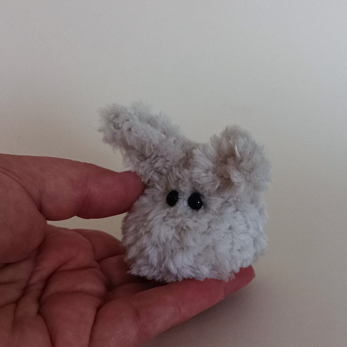 A small pocket sized handmade fuzzy worry bunny sitting in a person's palm to show the exact miniature scale. Perfect tactile anti stress fidget toy size overview.