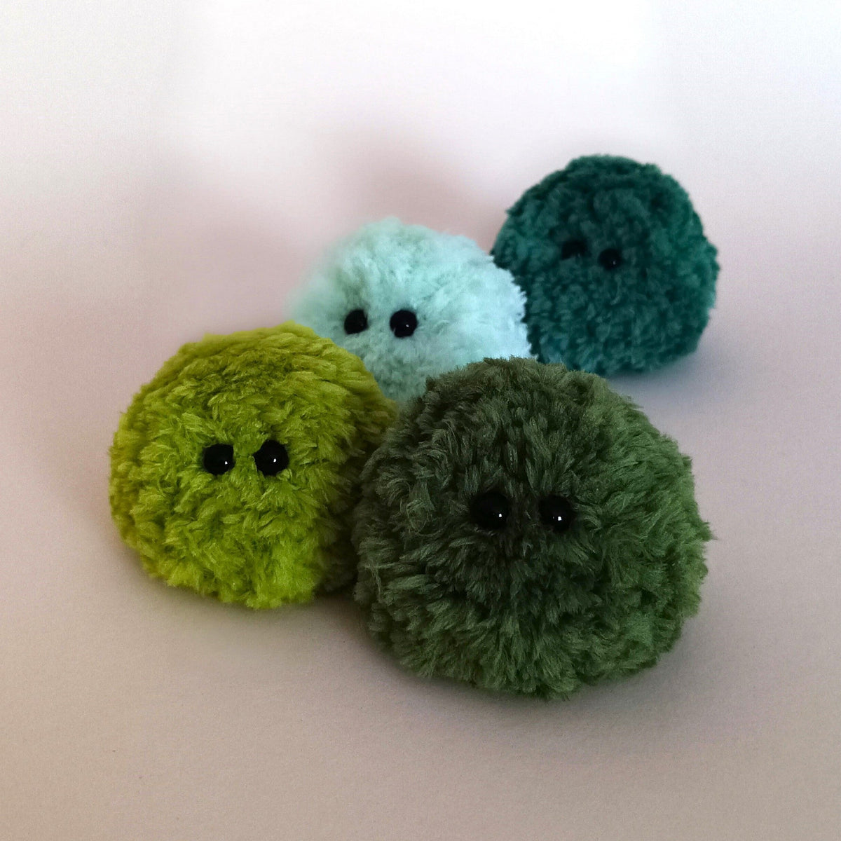 Four miniature fluffy moss plush friends in different shades of green, mint, and forest green. Perfect moss ball desk decor and cute desk pet set.