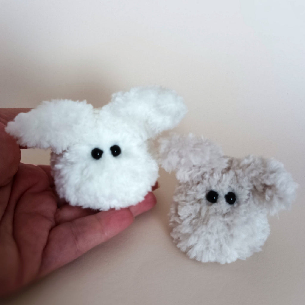 Two miniature ultra fluffy handmade worry pet bunnies in white and light grey colors sitting on a person's palm to show the pocket size scale. Small cute autumn or winter gift idea by PlushWhisper.