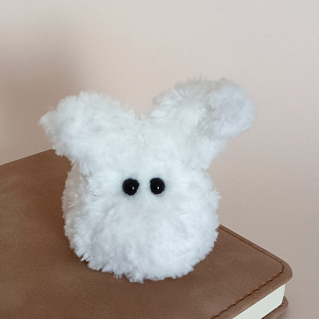 A tiny handmade white fuzzy bunny plush desk pet sitting on a brown leather planner next to a clean background. Minimalist winter office desk accessories and unique soft anxiety relief fidget toy for adults by PlushWhisper.