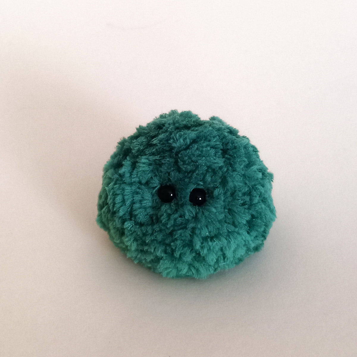 A single dark forest green miniature moss plush ball friend with small black eyes. Micro fairy core room decor accent and emotional support desk pet.