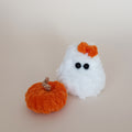 Tiny white crochet ghost with an orange bow beside a handmade orange pumpkin, cozy Halloween desk decor by PlushWhisper