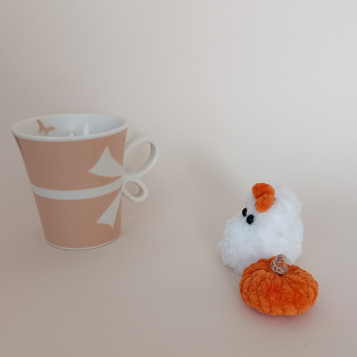 Tiny white crochet ghost with orange bow and handmade orange pumpkin beside a coffee cup, cozy Halloween desk decor