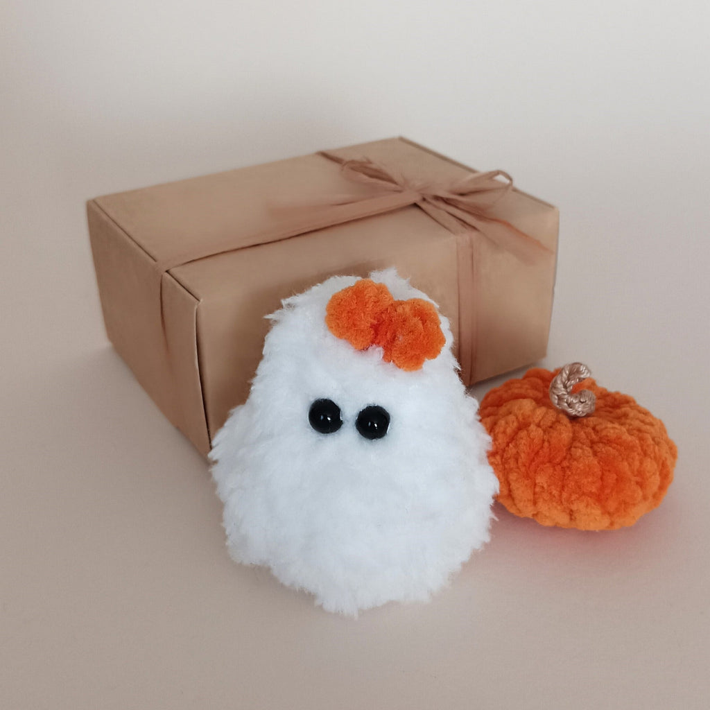 Tiny white crochet ghost with orange bow and matching orange pumpkin beside a kraft gift box, handmade Halloween gift set