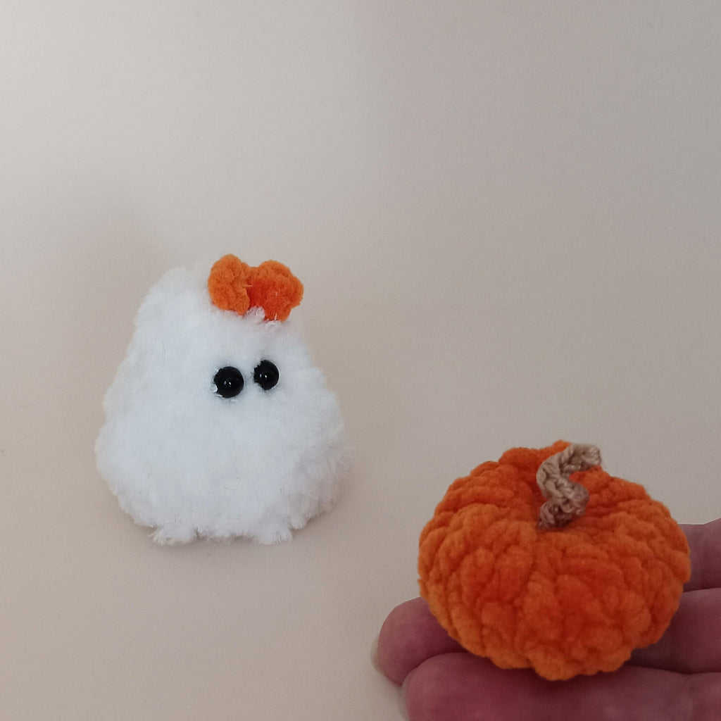 Tiny handmade orange crochet pumpkin held in hand beside a fluffy white ghost with orange bow, miniature Halloween decor