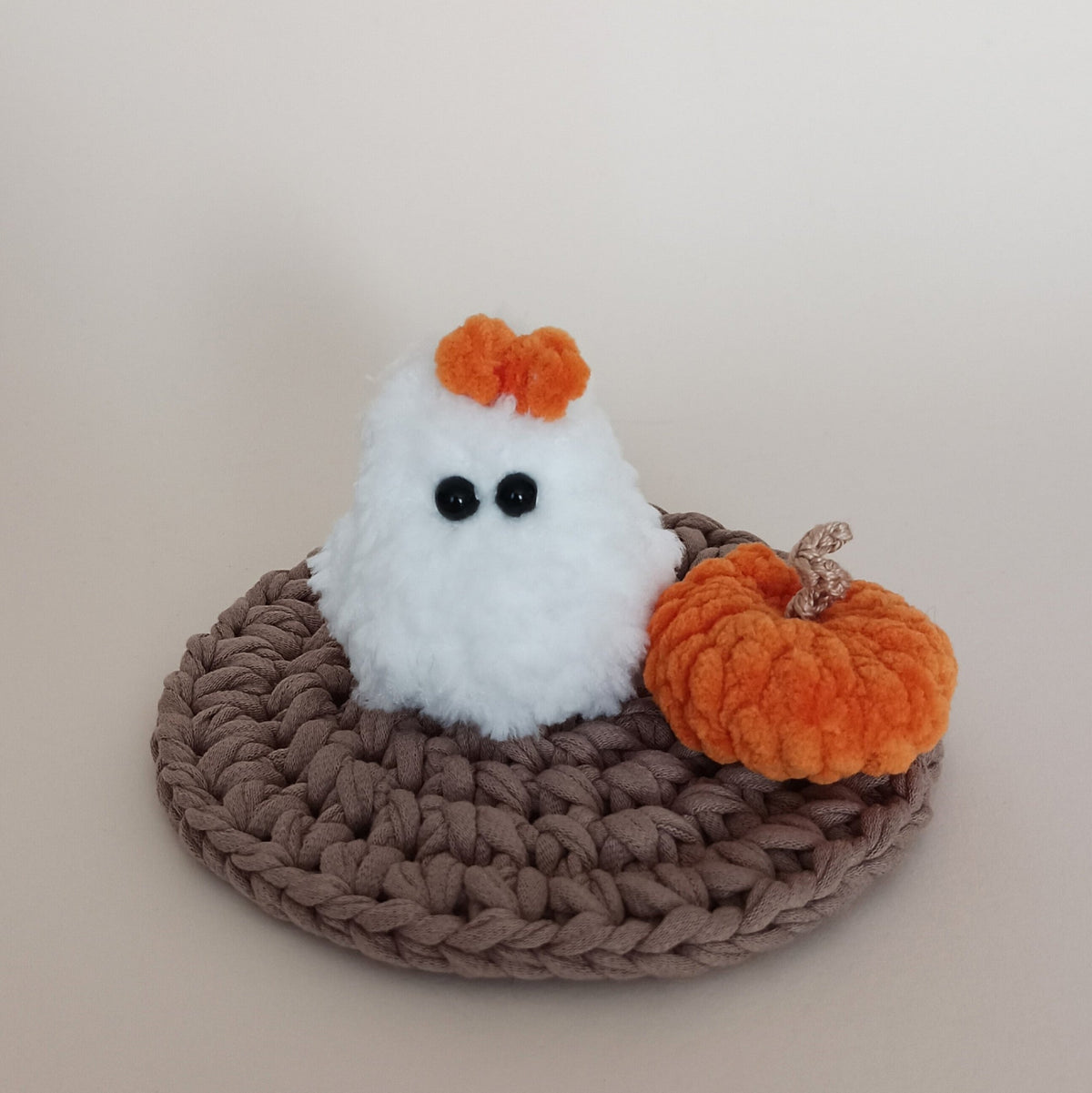 Fluffy white crochet ghost with orange bow and matching mini orange pumpkin displayed on a handmade crochet mat, cozy Halloween decor