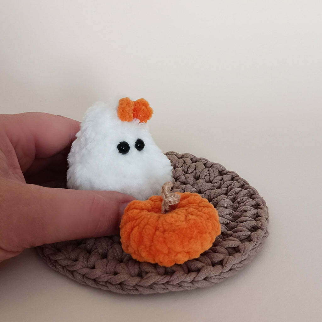 Tiny white crochet ghost with orange bow and mini orange pumpkin shown beside a hand for scale, handmade Halloween desk decor