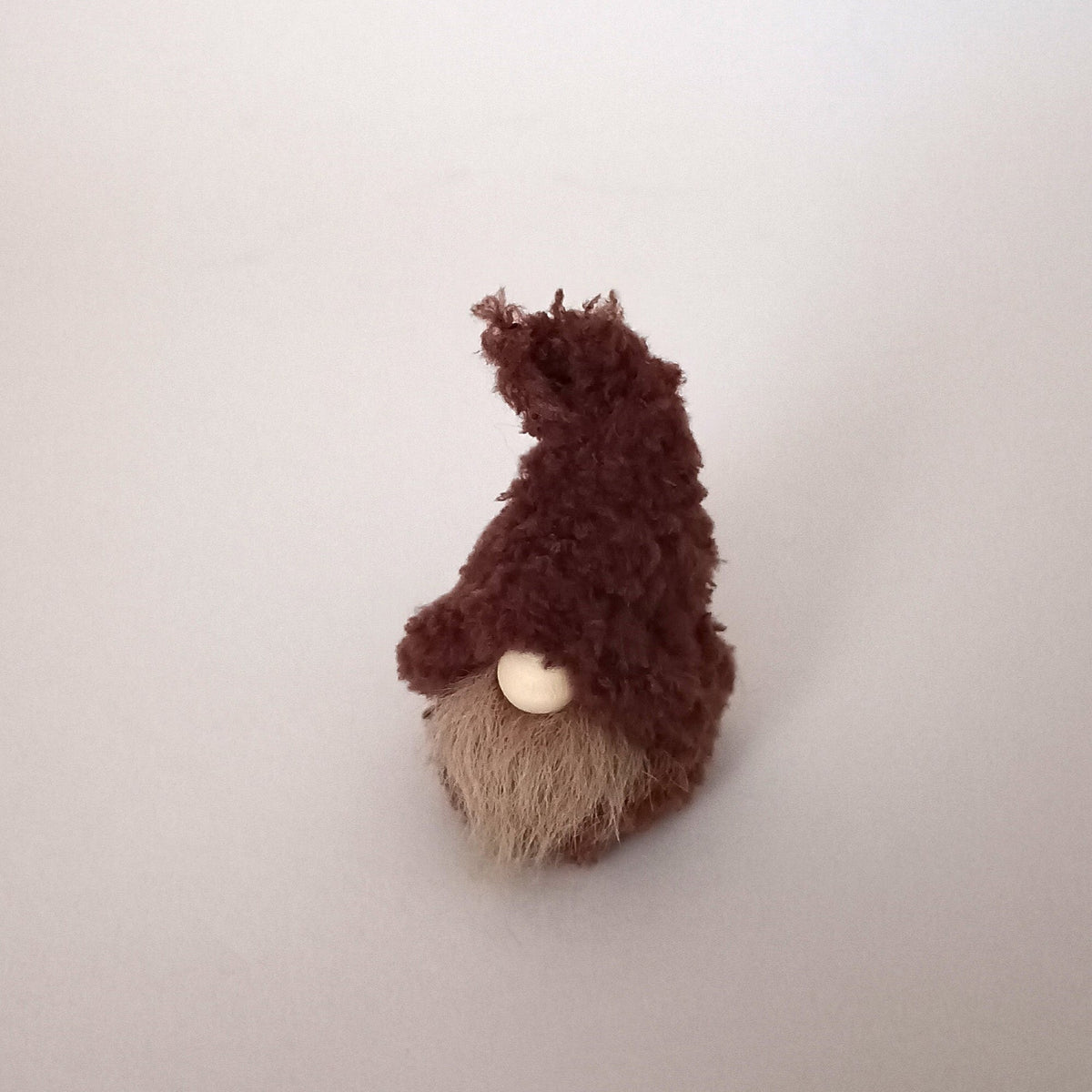 A miniature handmade espresso brown coffee gnome plush standing alone on a white background. Cute primitive textile desk pet ornament and tiny minimalist pocket buddy gift for coffee lovers.
