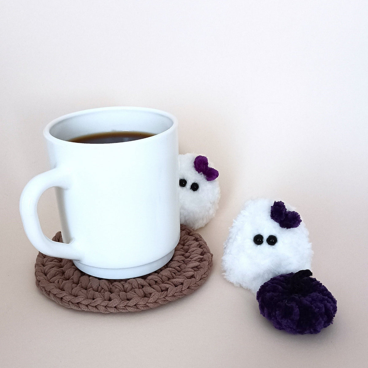 White handmade ghost with a purple bow and matching purple pumpkin beside a coffee mug, a tiny cozy Halloween desk decor set