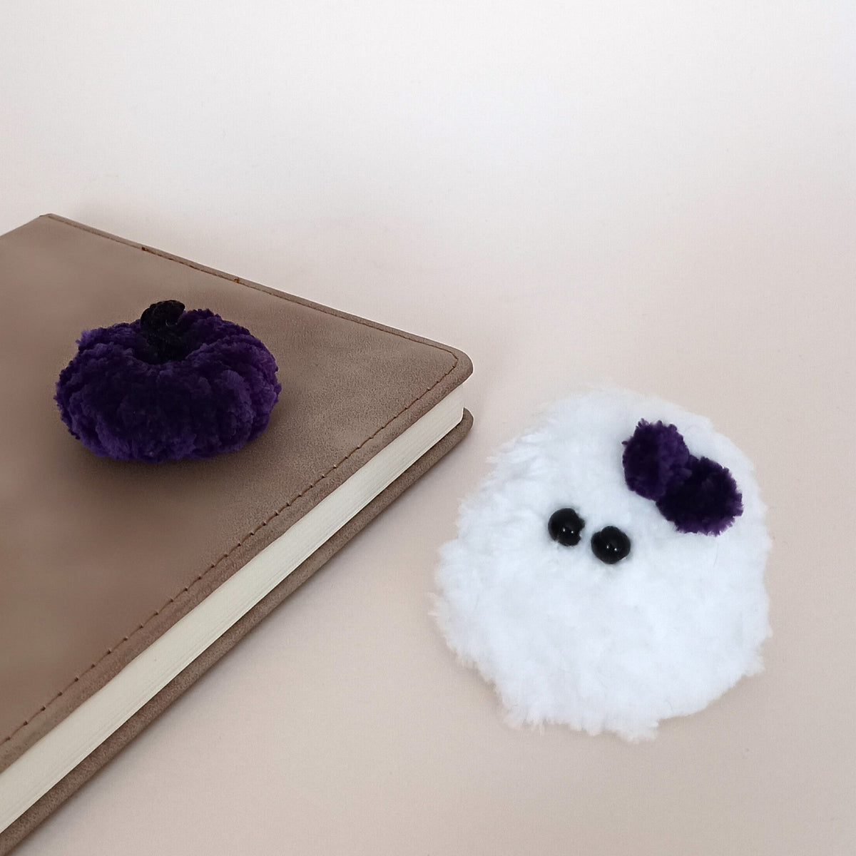White handmade ghost with a purple bow and matching purple pumpkin beside a notebook, a tiny cozy Halloween desk decor set