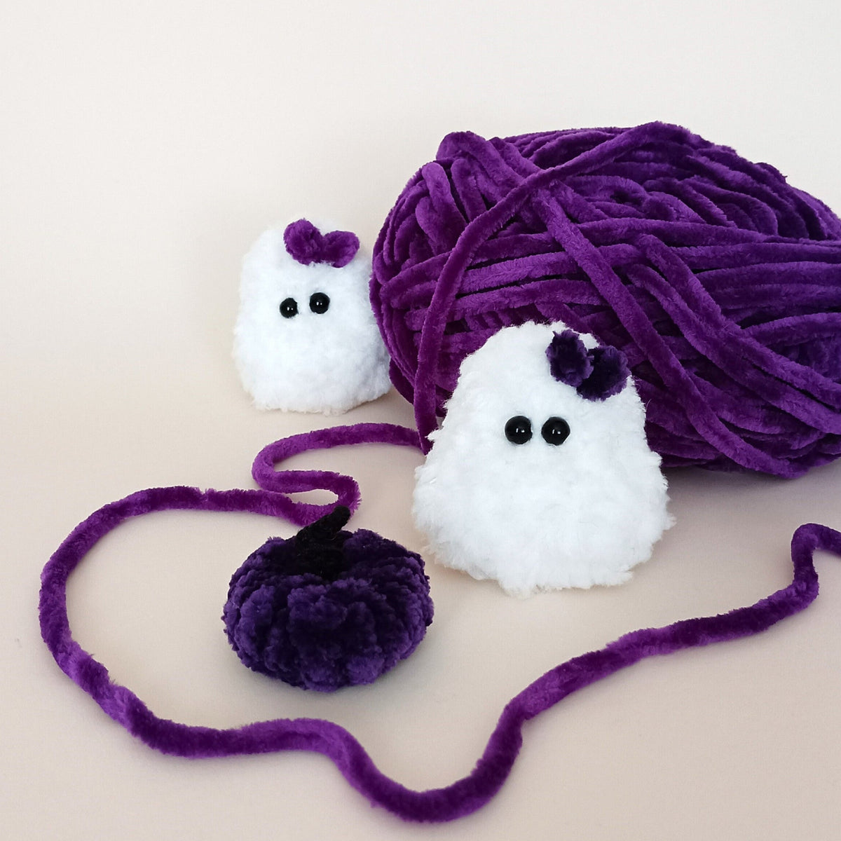 White handmade ghost with a purple bow and matching purple pumpkin displayed with purple yarn, a cozy handmade Halloween decor set