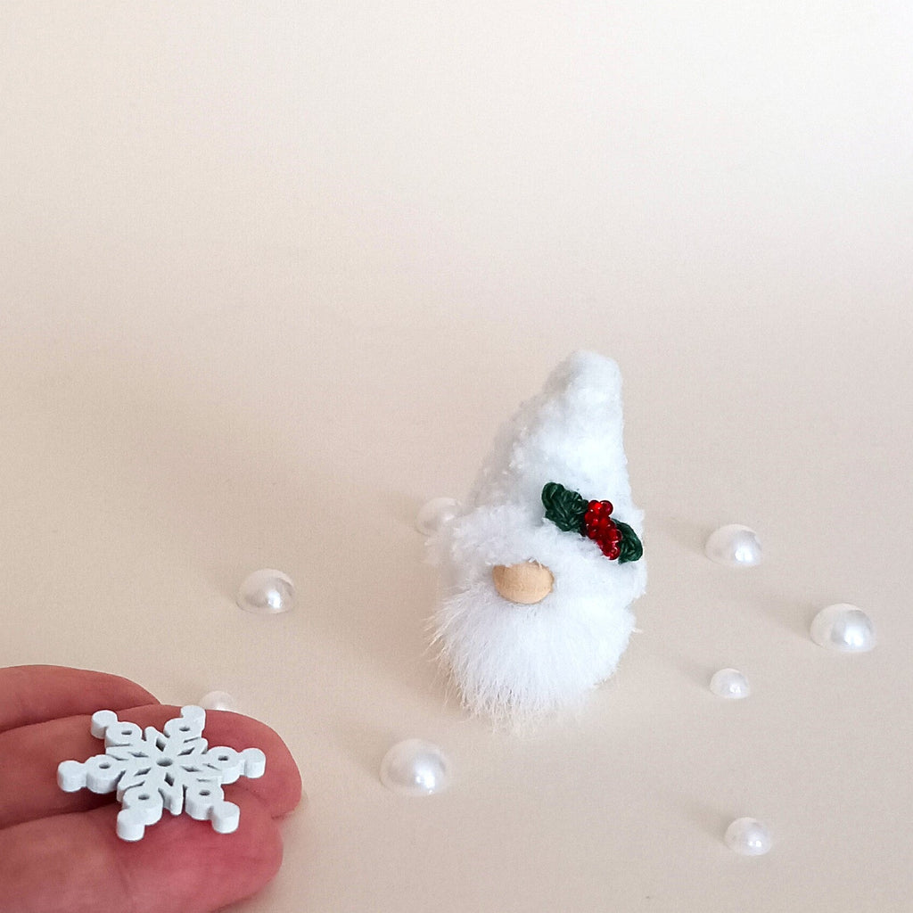 Miniature 2-inch Christmas pocket gnome next to pearl beads and a hand holding a tiny wooden snowflake, creating a magical winter aesthetic.
