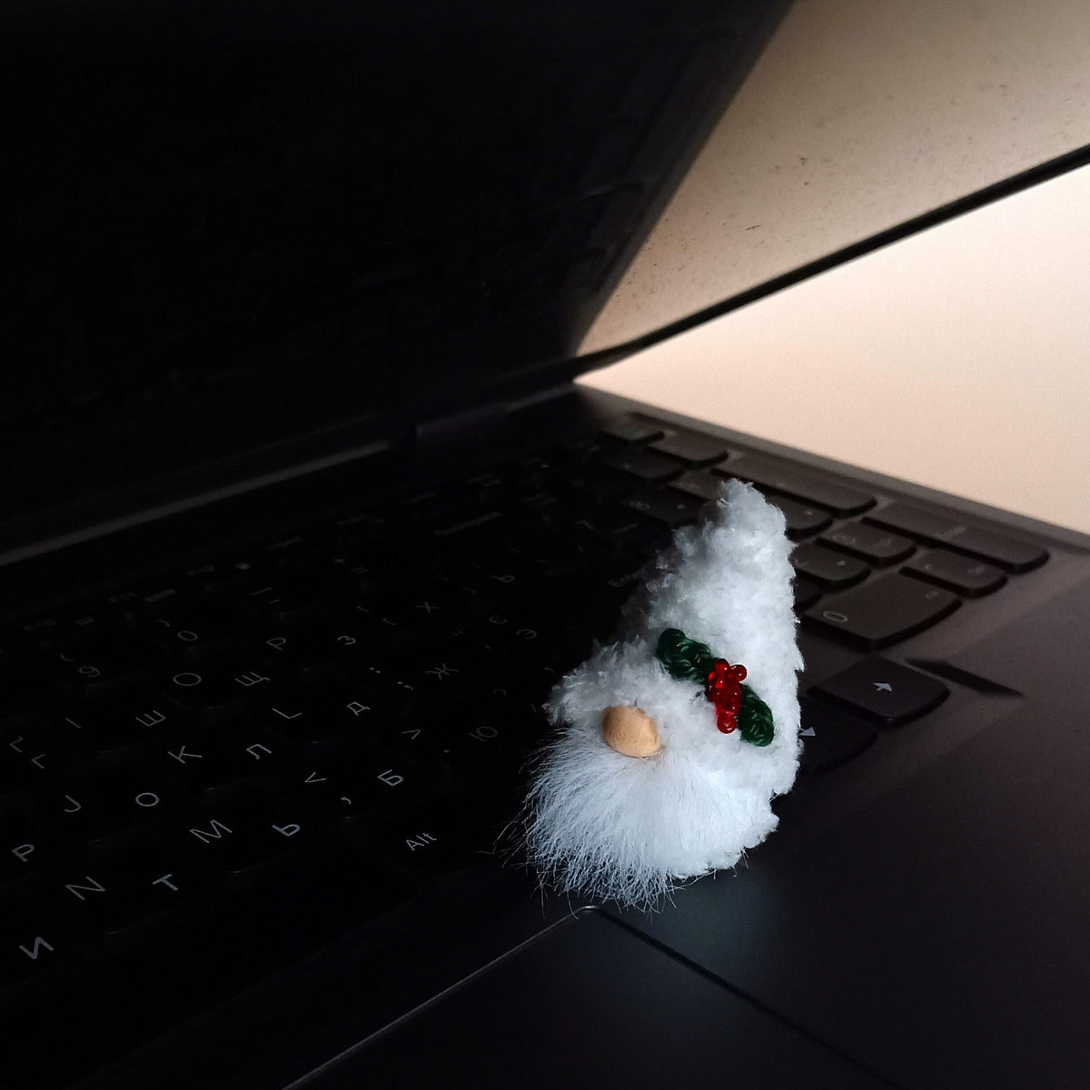 Tiny white Christmas plush gnome sitting on a laptop keyboard, perfect tech coworker gift and cute emotional support desk pet for work stress.