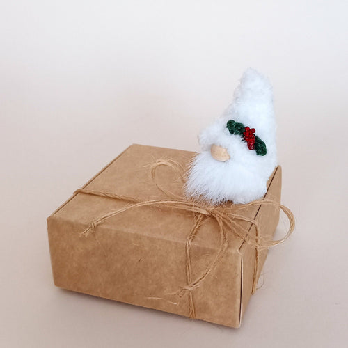 Miniature white Christmas plush gnome sitting on top of a closed craft gift box tied with twine string, showcasing minimalist holiday packaging ideas.