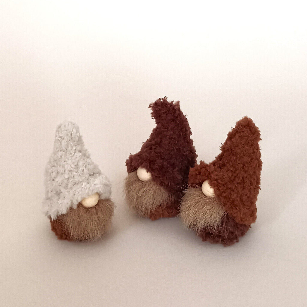 Three tiny handmade coffee gnome plushies in cream, cappuccino, and espresso brown colors standing together in a row on a white background. Cute set of minimalist desk pets and tiny woodland holiday gift ideas for coffee lovers.