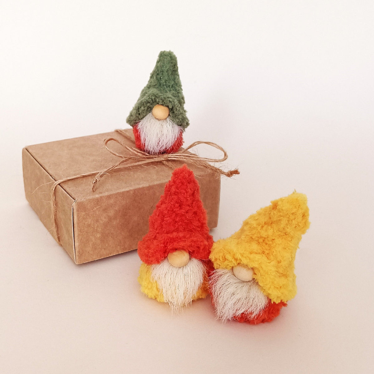 Desk Trio style option featuring three miniature handmade autumn gnomes in green, orange, and yellow boucle hats standing with a kraft gift box. Cozy primitive fall workspace decor and complete small office desk pet set gift for coworkers.