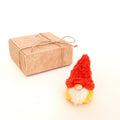 A tiny handmade pumpkin spice gnome plush standing next to a kraft paper gift box tied with a twine bow. Aesthetic minimalist packaging for a small autumn coworker gift and unique thinking of you treat.