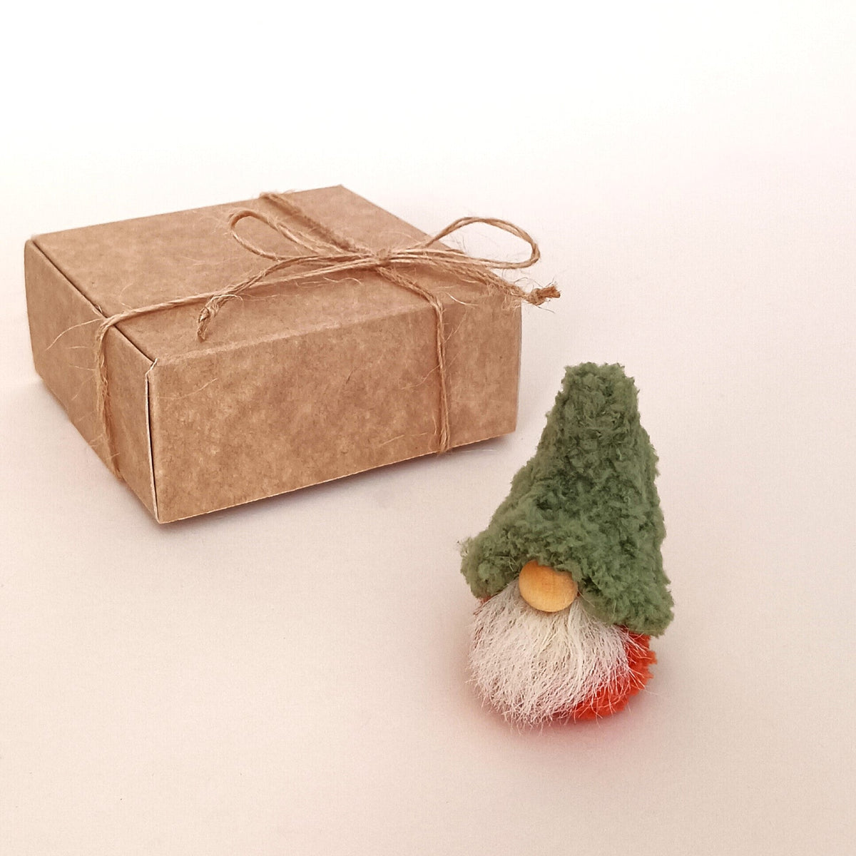 Forest moss green gnome style option standing next to a kraft paper gift box tied with a twine bow. Miniature primitive autumn desk pet variation and unique small holiday gift box idea for coworkers.