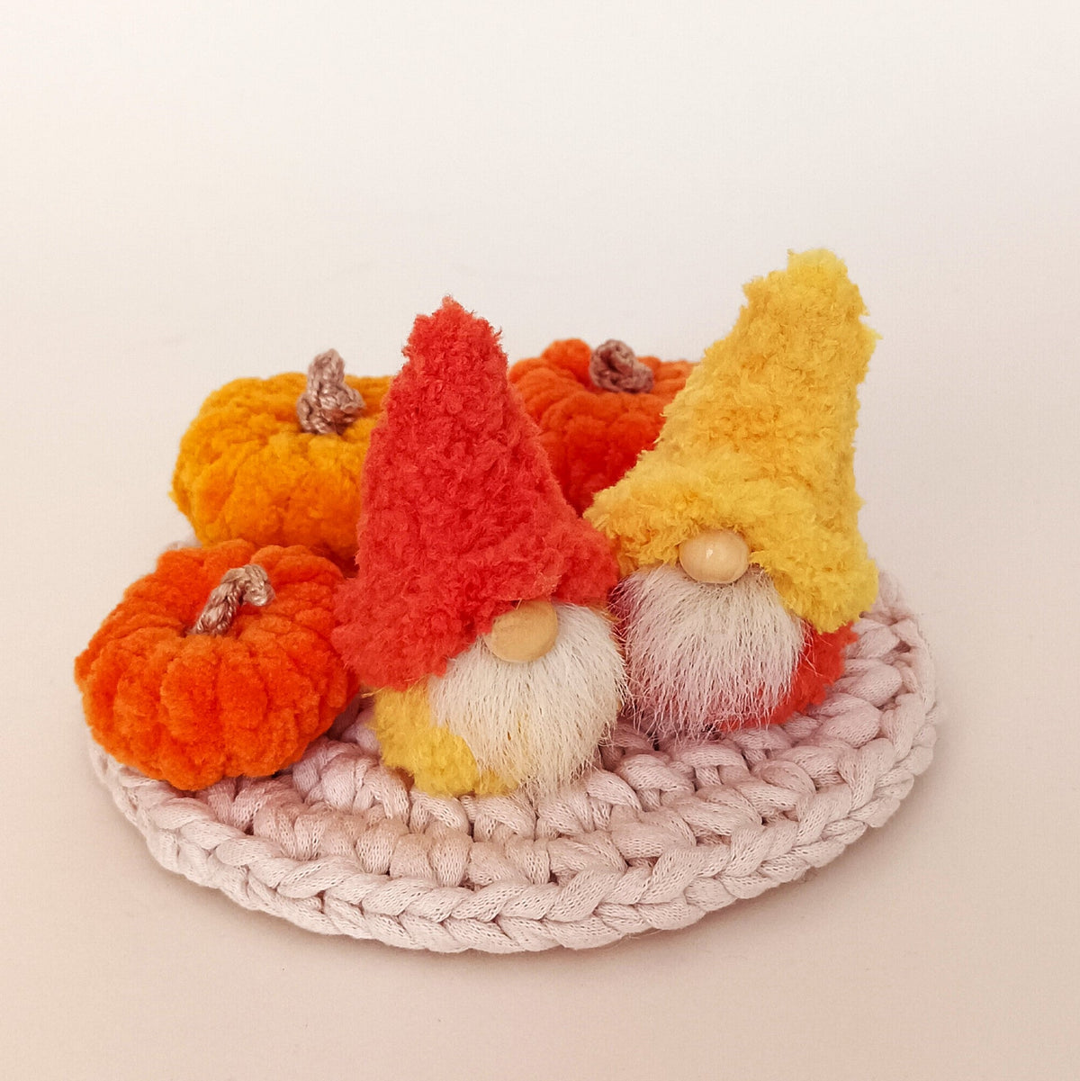 Cozy fall duo variation featuring two miniature handmade gnomes in orange and yellow hats sitting with plush pumpkins on a woven coaster. Small autumn home decor accents and cute tiered tray display gift package for adults.
