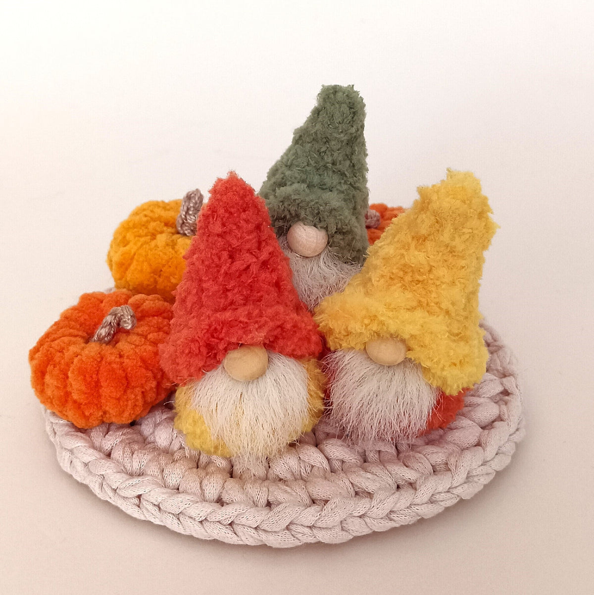 A full harvest set option showing three miniature handmade autumn gnomes in green, orange, and yellow boucle hats sitting with small crocheted pumpkins on a woven mat. Complete fall tiered tray decor and cozy Thanksgiving gift idea for adults.